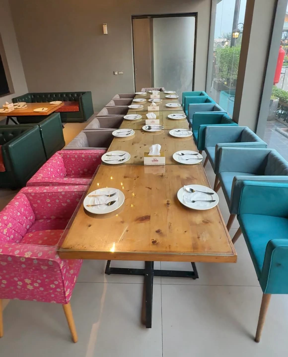 Long wooden dining table set with plates beside turquoise and patterned upholstered chairs