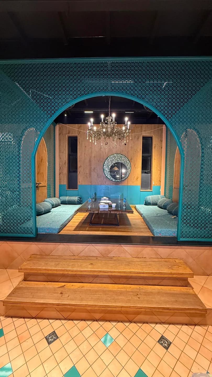 Turquoise carved arch framing floor cushions, a low dining table, and a chandelier