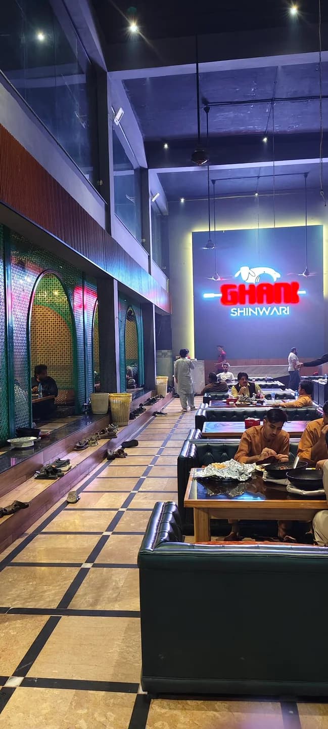 Indoor dining hall with upholstered seating, patterned partitions, and an illuminated Ghani Shinwari sign